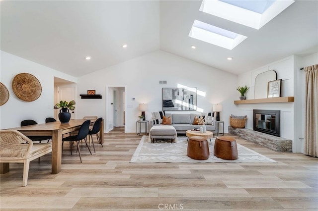 living room featuring a skylight, a fireplace, high vaulted ceiling, and light wood-type flooring