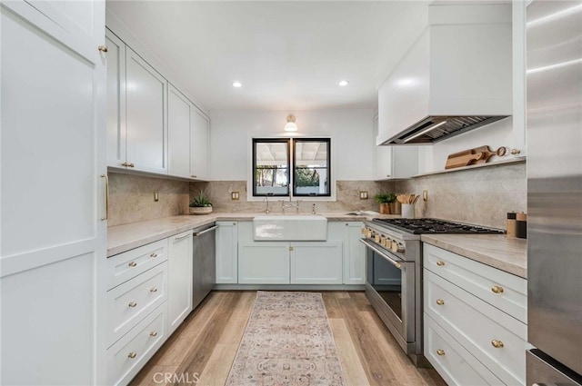 kitchen featuring premium range hood, white cabinets, sink, light hardwood / wood-style floors, and stainless steel appliances