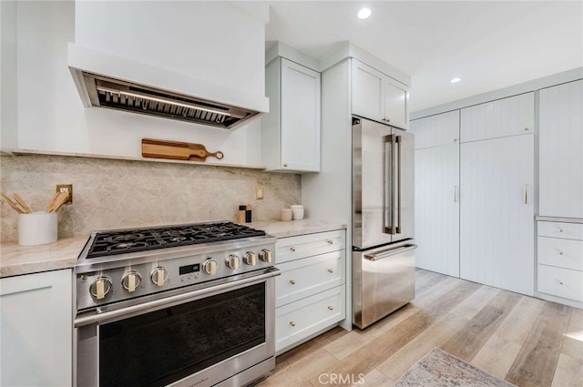 kitchen with appliances with stainless steel finishes, backsplash, custom range hood, light hardwood / wood-style floors, and white cabinetry