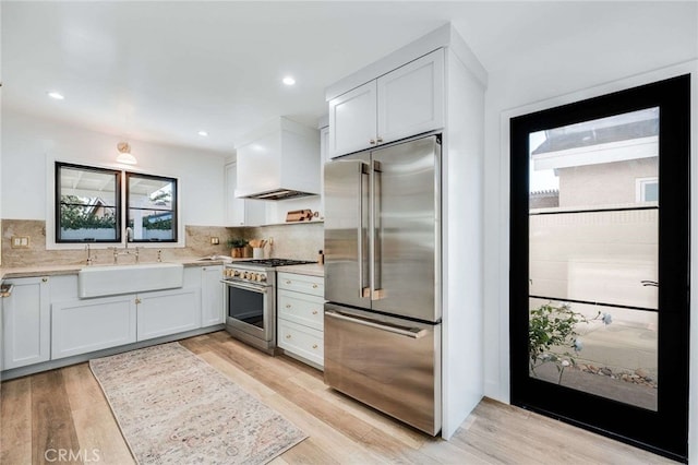 kitchen with high quality appliances, sink, white cabinets, and custom range hood