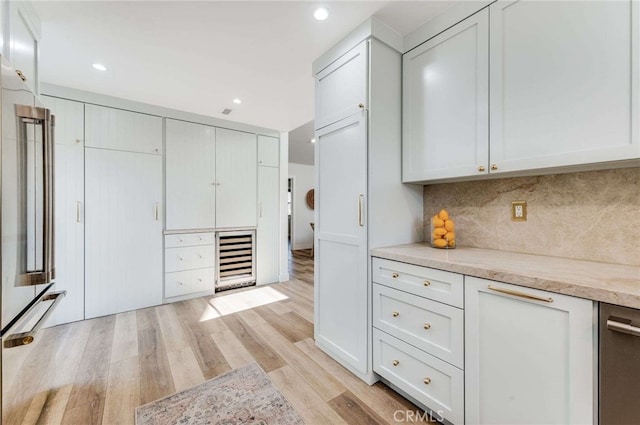 kitchen with tasteful backsplash, light stone counters, white cabinets, and light hardwood / wood-style floors