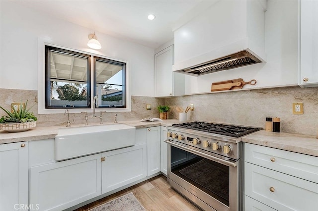 kitchen with custom range hood, stainless steel range with gas cooktop, sink, light hardwood / wood-style floors, and white cabinetry