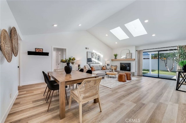 dining space with a skylight, light hardwood / wood-style flooring, high vaulted ceiling, and a fireplace