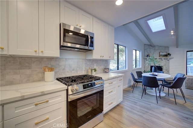 kitchen with lofted ceiling with skylight, white cabinets, light stone countertops, tasteful backsplash, and stainless steel appliances