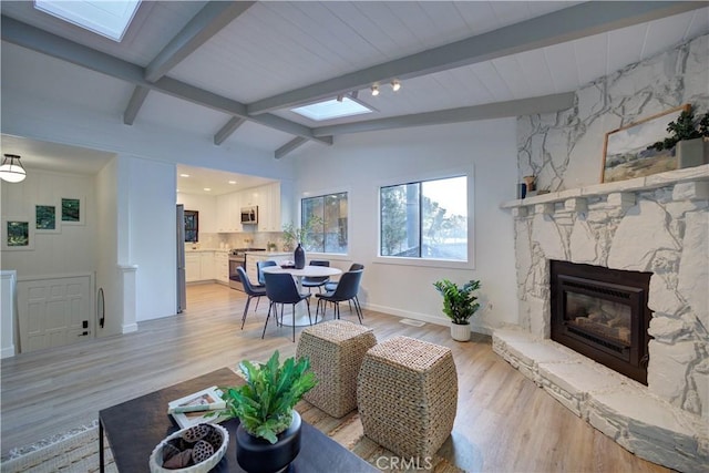 living room featuring light wood-type flooring, a stone fireplace, and lofted ceiling with skylight