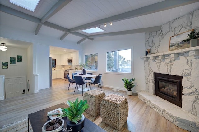 living area with light wood-type flooring, vaulted ceiling with skylight, a fireplace, and baseboards