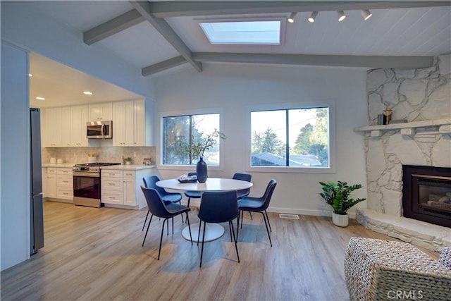 dining space with light wood-type flooring, lofted ceiling with skylight, and a stone fireplace