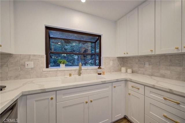 kitchen with tasteful backsplash, white cabinetry, sink, and light stone counters