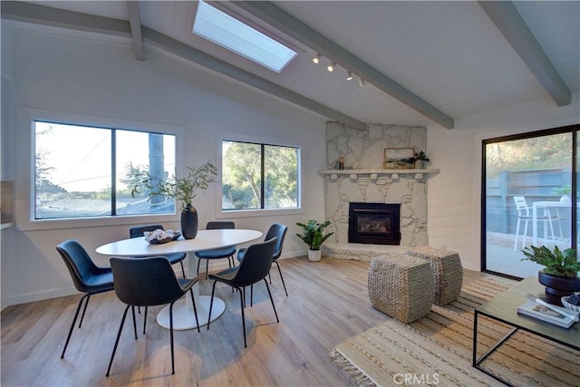 dining area featuring vaulted ceiling with skylight, a fireplace, and light hardwood / wood-style flooring