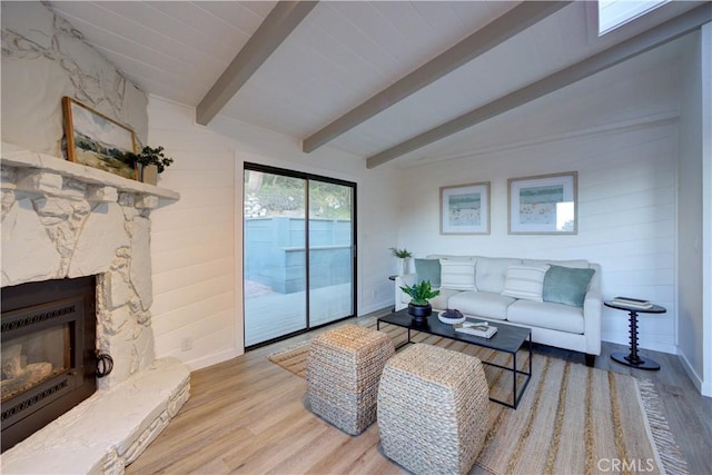 living area featuring vaulted ceiling with beams, a fireplace, wood finished floors, and baseboards