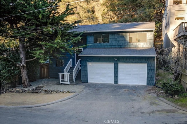 view of front of home with driveway, a shingled roof, stairway, an attached garage, and fence