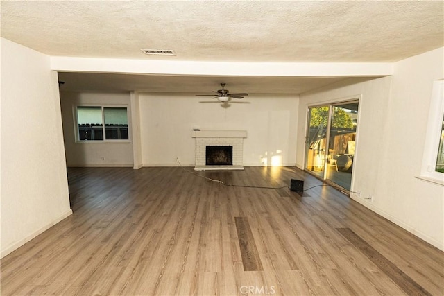 unfurnished living room with light hardwood / wood-style flooring, a textured ceiling, a fireplace, and ceiling fan