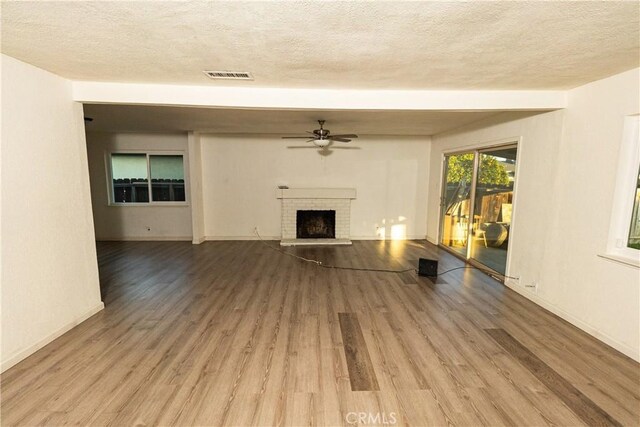 unfurnished living room featuring light hardwood / wood-style flooring, a textured ceiling, a fireplace, and ceiling fan