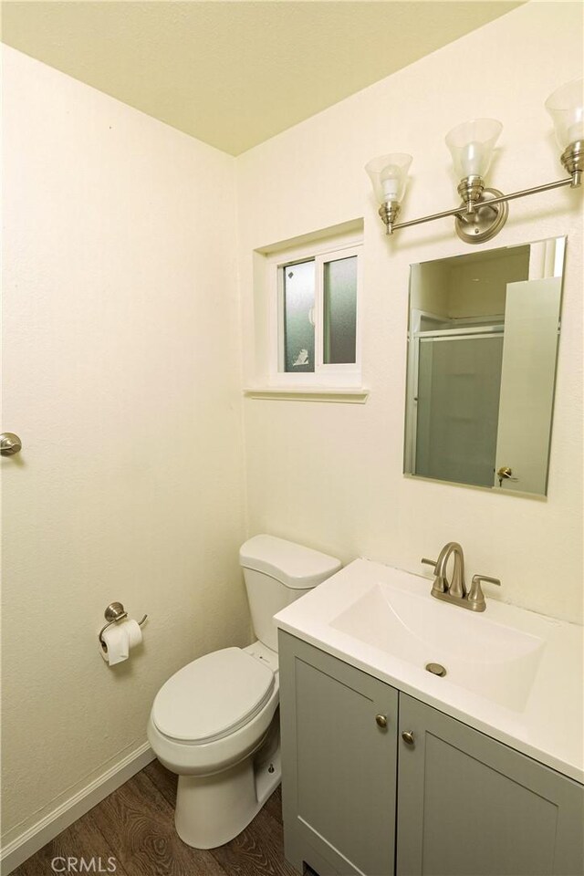 bathroom featuring vanity, wood-type flooring, a shower with shower door, and toilet