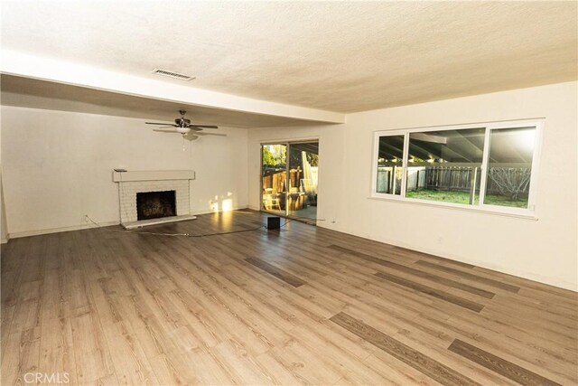 unfurnished living room with ceiling fan, a fireplace, light hardwood / wood-style floors, and a textured ceiling