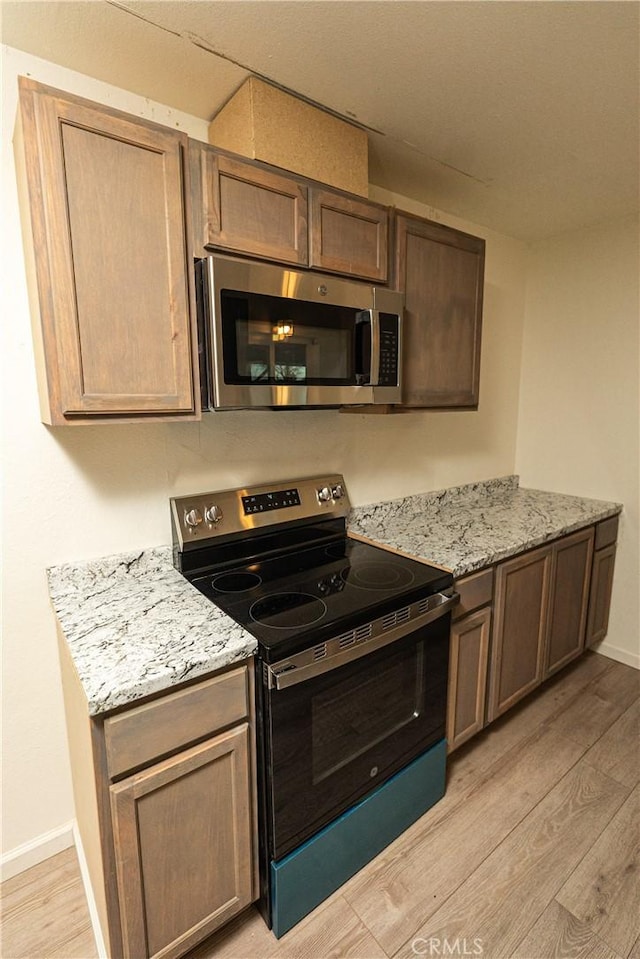 kitchen featuring stainless steel appliances, light stone countertops, and light wood-type flooring