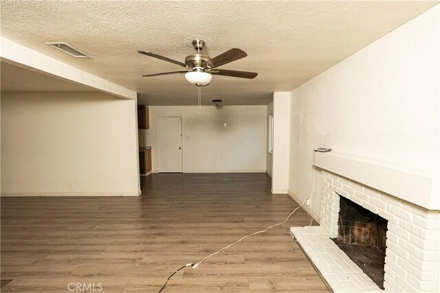 unfurnished living room with ceiling fan, wood-type flooring, a fireplace, and a textured ceiling