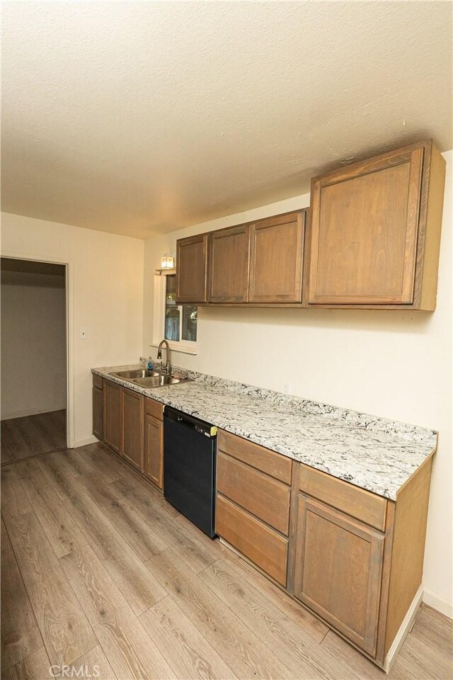 kitchen featuring light stone countertops, black dishwasher, sink, and light hardwood / wood-style flooring