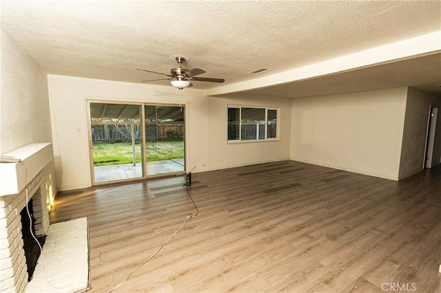 unfurnished living room featuring a brick fireplace, hardwood / wood-style floors, a textured ceiling, and ceiling fan