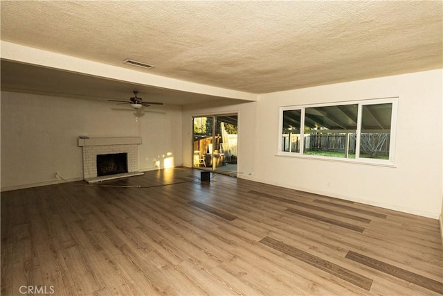 unfurnished living room featuring a brick fireplace, a wealth of natural light, hardwood / wood-style floors, and a textured ceiling