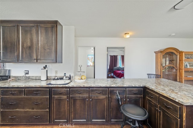 kitchen with a breakfast bar area, light stone countertops, a textured ceiling, dark brown cabinetry, and sink