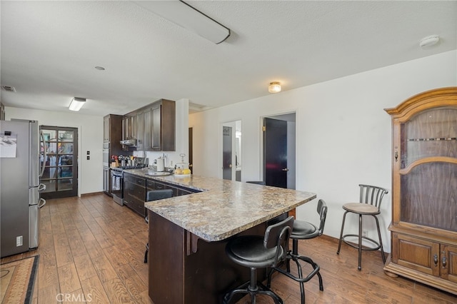 kitchen with a breakfast bar, dark brown cabinetry, dark wood-type flooring, a textured ceiling, and stainless steel appliances