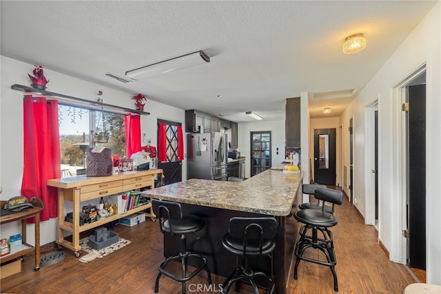 kitchen featuring a textured ceiling, a kitchen breakfast bar, stainless steel fridge, dark hardwood / wood-style floors, and kitchen peninsula