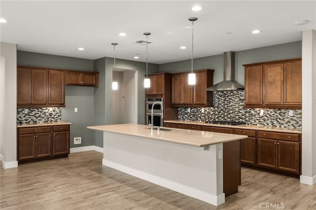 kitchen featuring stainless steel appliances, an island with sink, pendant lighting, and wall chimney range hood