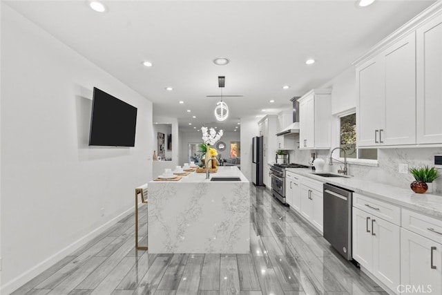 kitchen with stainless steel appliances, a sink, white cabinetry, decorative backsplash, and wall chimney exhaust hood