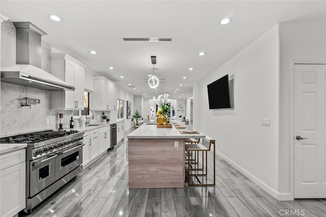 kitchen with stainless steel appliances, decorative backsplash, white cabinetry, a kitchen island, and wall chimney range hood