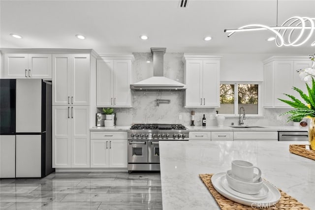 kitchen featuring appliances with stainless steel finishes, white cabinetry, a sink, and wall chimney range hood