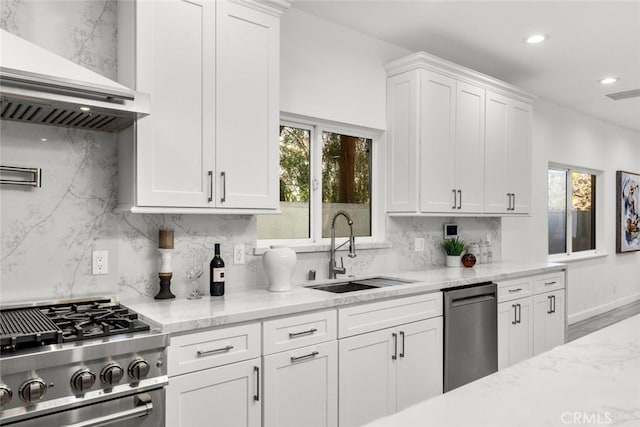 kitchen featuring stainless steel appliances, a sink, white cabinetry, wall chimney range hood, and tasteful backsplash