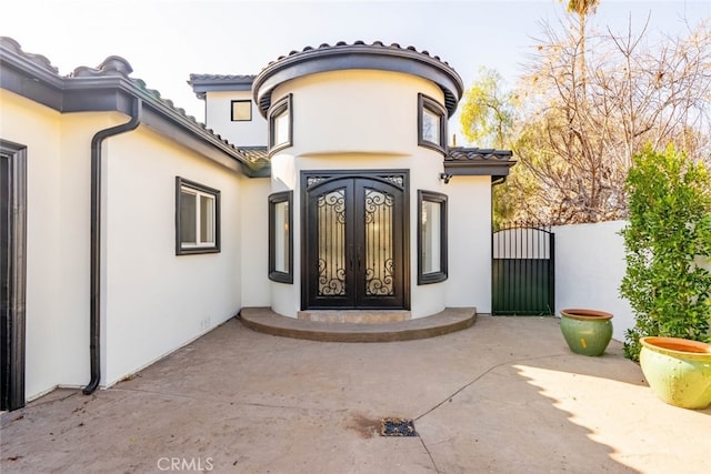 view of exterior entry featuring a tile roof, a gate, french doors, and stucco siding