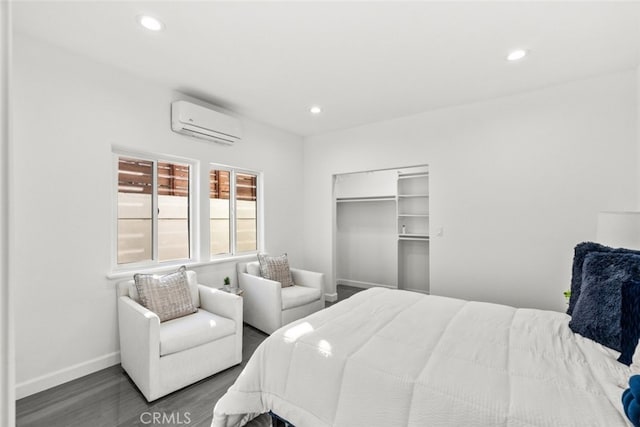 bedroom featuring a wall unit AC, baseboards, wood finished floors, and recessed lighting