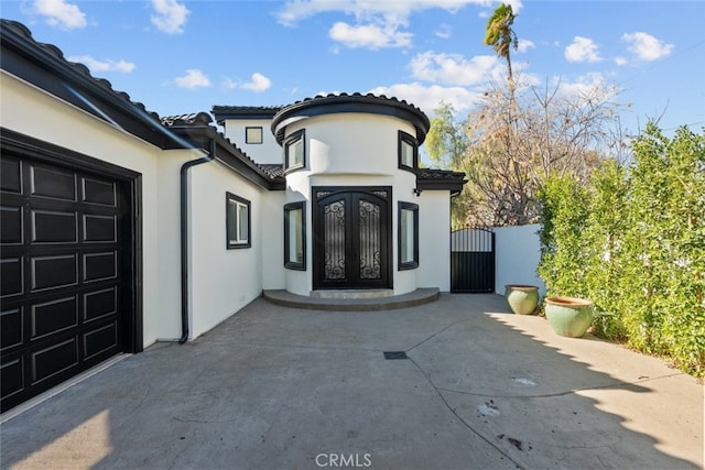 doorway to property with a garage, stucco siding, a gate, and french doors