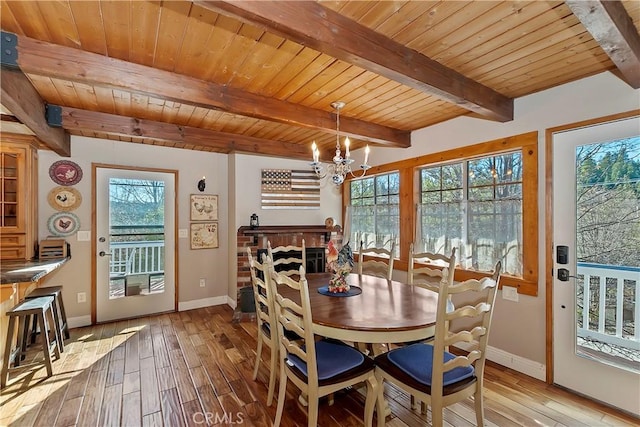 dining room with a chandelier, wood ceiling, a brick fireplace, light wood-type flooring, and beamed ceiling