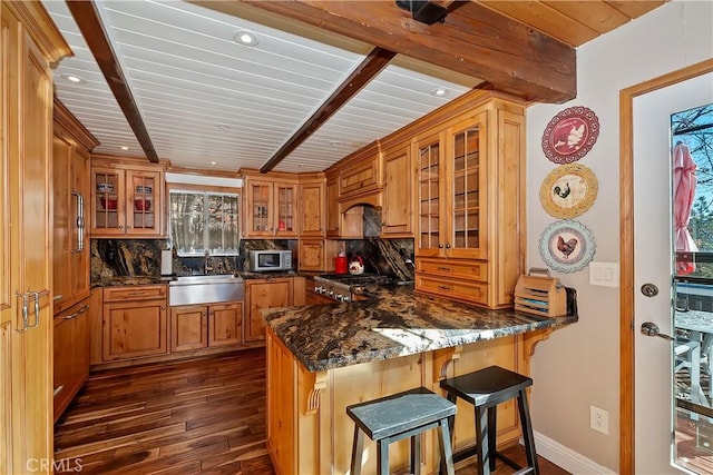 kitchen featuring a breakfast bar area, tasteful backsplash, dark stone counters, and kitchen peninsula