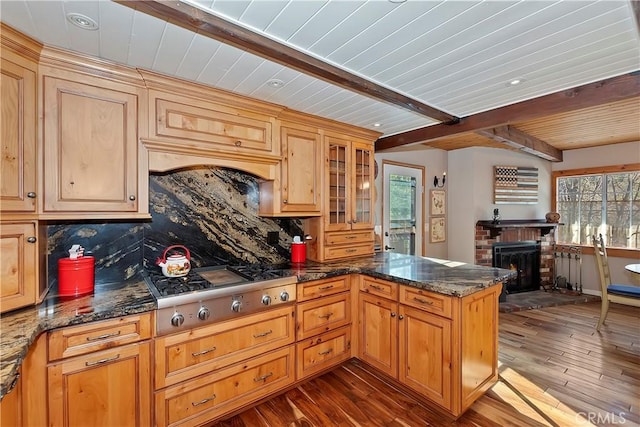 kitchen with a fireplace, stainless steel gas cooktop, backsplash, and beamed ceiling