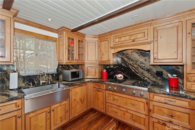 kitchen featuring dark wood-type flooring, backsplash, dark stone counters, appliances with stainless steel finishes, and sink