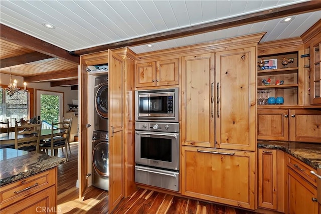 kitchen with dark stone counters, stacked washer and clothes dryer, a notable chandelier, and appliances with stainless steel finishes