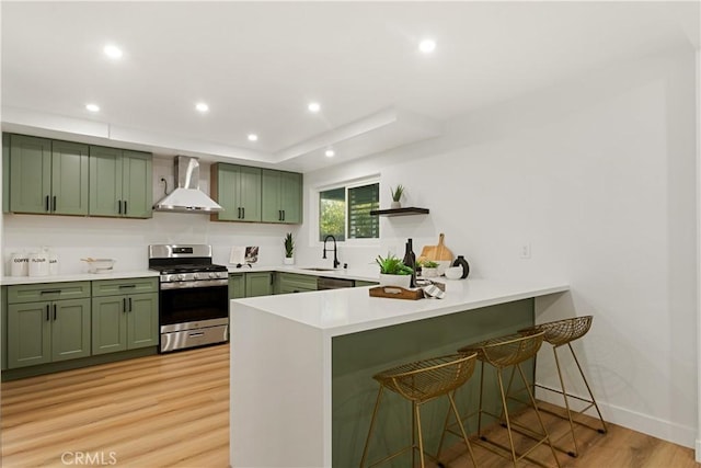 kitchen with gas range, sink, wall chimney range hood, light hardwood / wood-style floors, and green cabinetry