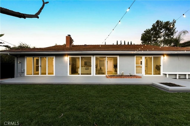 back house at dusk with a yard and a patio