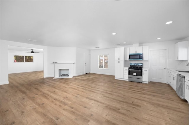 unfurnished living room with ceiling fan, sink, light wood-type flooring, and a brick fireplace