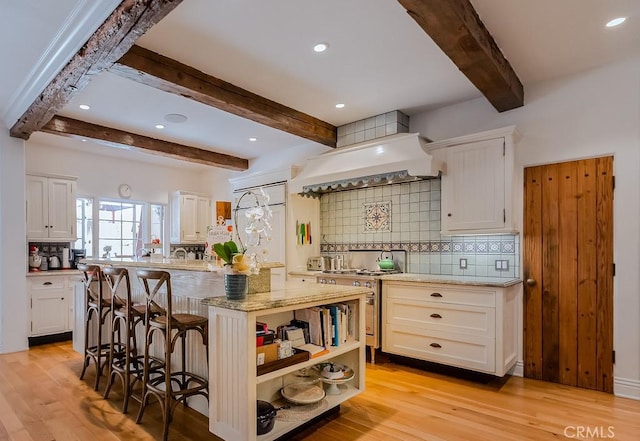 kitchen featuring premium range hood, a center island, a breakfast bar, decorative backsplash, and white cabinets