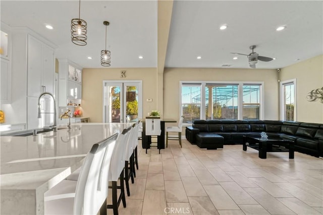 interior space with ceiling fan, sink, decorative light fixtures, a kitchen bar, and white cabinets