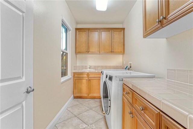 washroom featuring a sink, cabinet space, washing machine and clothes dryer, light tile patterned floors, and baseboards