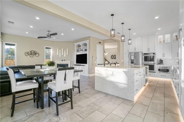 kitchen featuring hanging light fixtures, white cabinetry, a kitchen island with sink, and double oven