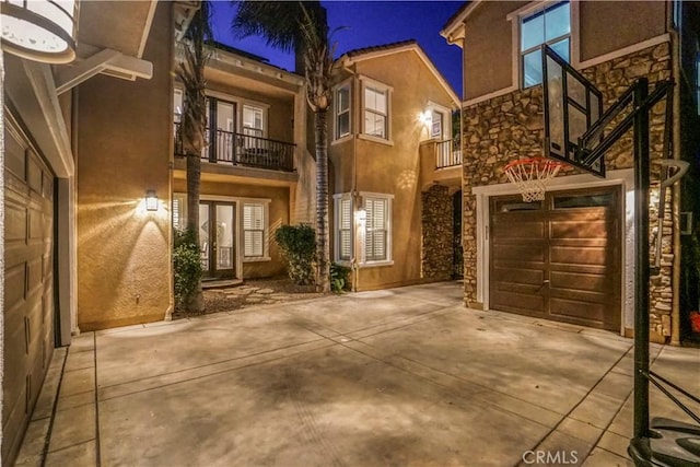 exterior space with stucco siding, driveway, a balcony, and stone siding