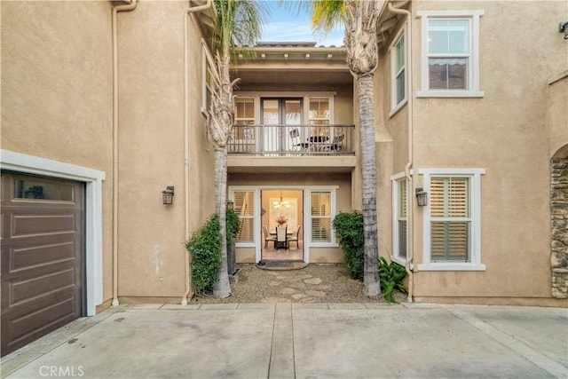 entrance to property featuring a garage, stucco siding, and a balcony