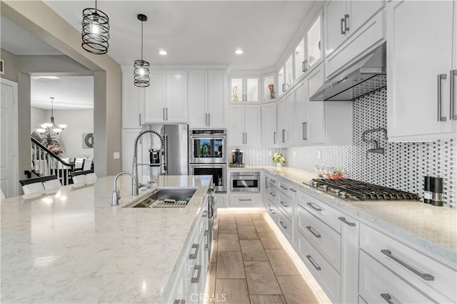 kitchen with white cabinetry, sink, light stone countertops, hanging light fixtures, and tasteful backsplash